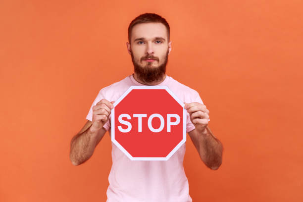 istock Man holding red stop sign looking at camera with serious expression. 1383882083