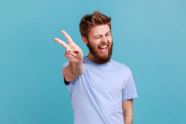 istock Man doing victory gesture, winking playfully to camera, showing peace, v sign with double fingers. 1383882155