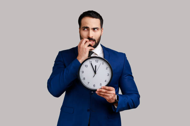 istock Nervous bearded man biting nails holding big wall clock, deadline, need hurry up. 1383882261