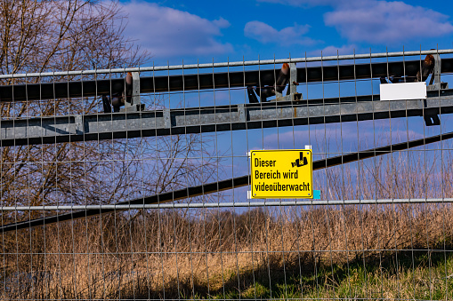 Warning sign on a fence of a company premises with German text that the area is under video surveillance