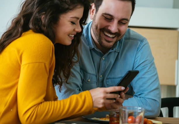 istock Happy Couple Using Mobile Phone and Laughing Together While Eating Breakfast at Home 1383886922