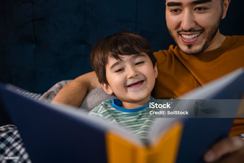 I Love This Story An Asian man and his young son wearing pyjamas in his bedroom on a winter's night. They are lying in bed while the father reads his son a bedtime story. Child Stock Photo