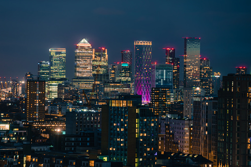 Aerial panoramic view of The City of London Canary Wharf cityscape skyline with metropole financial district modern skyscrapers after sunset on night with illuminated buildings and cloudy sky in London, UK