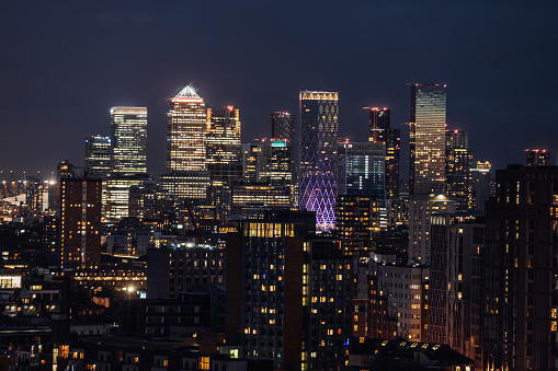 Aerial panoramic view of The City of London Canary Wharf cityscape skyline with metropole financial district modern skyscrapers after sunset on night with illuminated buildings and cloudy sky in London, UK