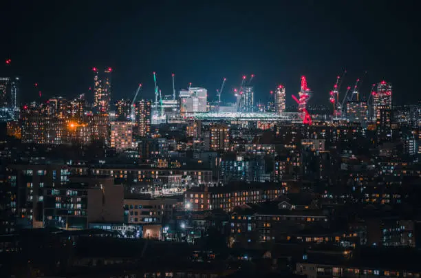 Aerial panoramic view of East London cityscape skyline with metropole Stratford, Westfield and Olympic Stadium after sunset on night with illuminated buildings and cloudy sky in London, UK