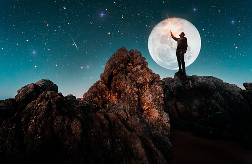 man standing on the rock outdoors contemplating the starry night and full Moon