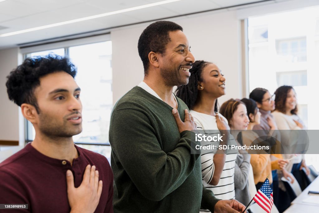 Class stands and recites The class stands to recite the Pledge of Allegiance with their hands on their hearts. Emigration and Immigration Stock Photo