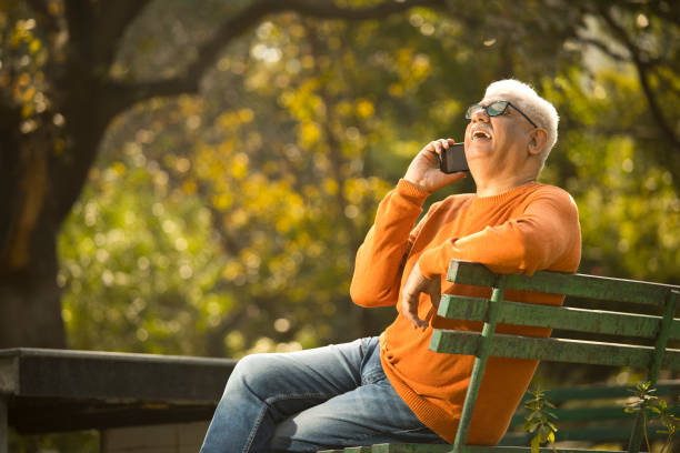 old man using mobile phone at park - using phone garden bench imagens e fotografias de stock