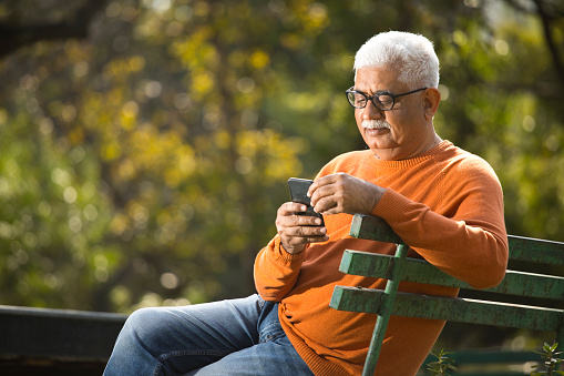 Happy senior man having fun using mobile phone at park
