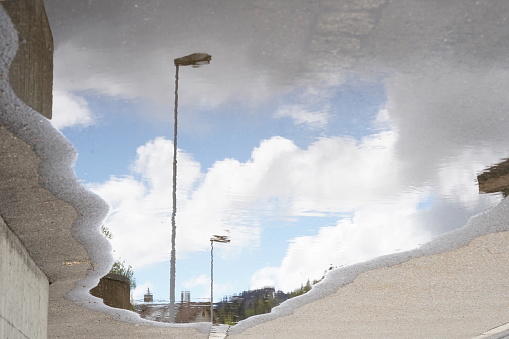 Street lamps and sky reflected in a puddle on the ground.