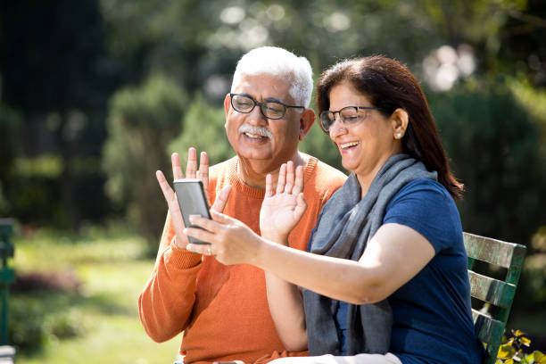 senior couple on video call at park - using phone garden bench imagens e fotografias de stock