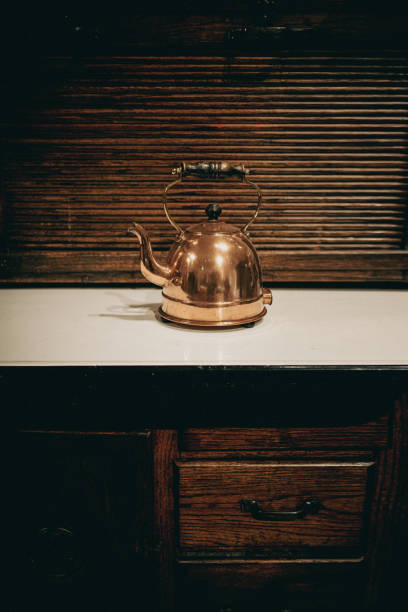 Antique old copper kettle sat on white kitchen surface with a wooden base with drawers