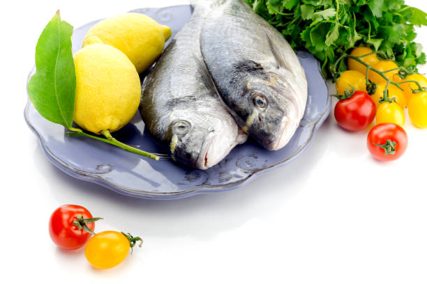 Fish sea breams(Sparus aurata) on a plate, lemons and cherry tomatoes on a white background close-up