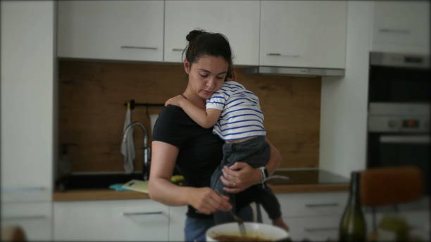 Mother cooking while holding baby toddler child stock photo