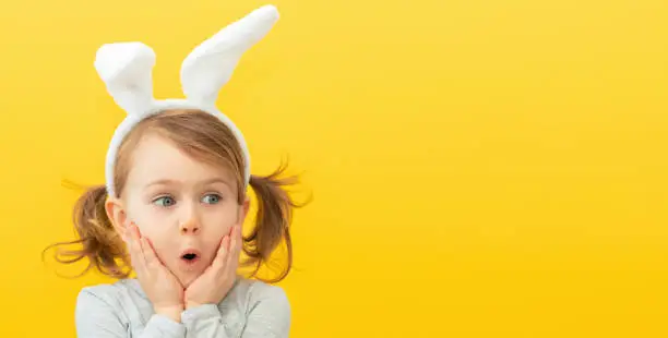 Photo of Seasonal sale and discount. Shopping and retail. Preparing for holiday. Promoting goods. Funny, surprise, little child girl in bunny ears. Banner, copy space for text, mock up. Spring, Easter concept.