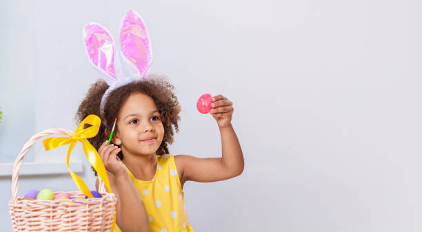 istock Little Black girl with bunny ears paint Easter eggs 1383952542