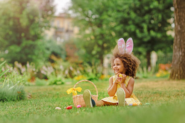 piccola ragazza nera che wtfring orecchie di coniglio raccogliendo uova di pasqua - easter easter egg child chocolate foto e immagini stock