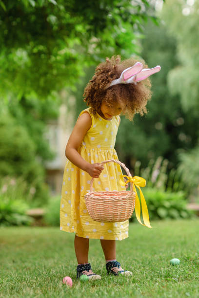 istock Little Black girl with bunny ears gathering Easter eggs 1383952551