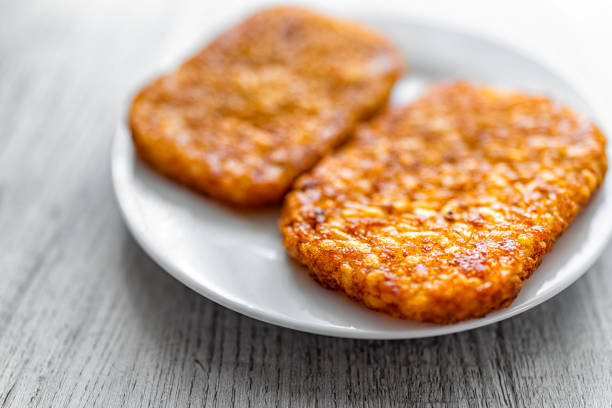 makro-nahaufnahme von frühstück oder brunch kartoffel gebratene zwei hash browns knusprige textur auf weißem teller mit holztischhintergrund - hash brown stock-fotos und bilder