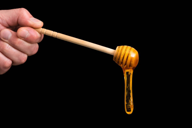istock Liquid honey drips from a wooden spoon on a black background. 1383958011
