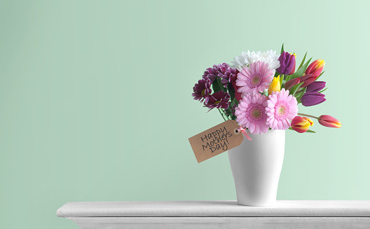 Mothers day spring flowers inside a pot on top of a fireplace mantelpiece with label