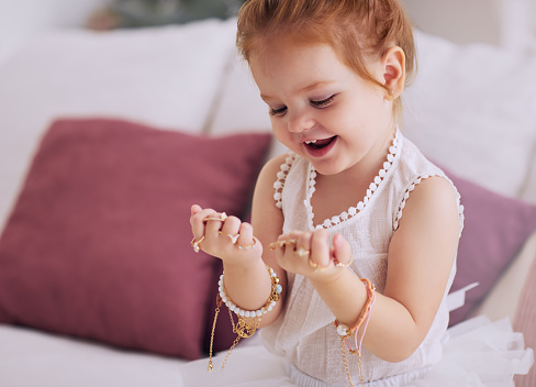 cute baby girl feeling happy trying on a lot of finger rings and bracelets, bijou jewelry