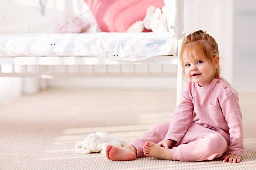 cute toddler baby girl sitting on the carpet in the nursery room