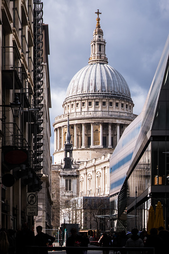 The iconic dome of St. Paul’s Cathedral illuminated by sunlight between the shopfronts and restaurants of the City of London Financial District, UK.