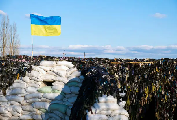 Ukrainian flag blue yellow color flutters in blue sky on barricades. Ukraine Russia War 2022. Freedom, democracy and independence symbol.