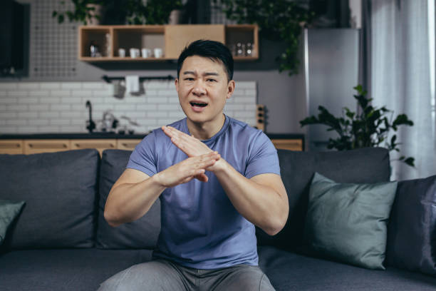 istock man talking on webcam, angry gesturing with hands, asian looking at camera, online call sitting on sofa at home 1383967576