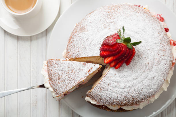 Top view of Victoria sponge cake with a cup of coffee Top view of Victoria sponge cake filled with strawberries, jam and whipped cream decorated with icing sugar and strawberry on a white wooden table sprinkling powdered sugar stock pictures, royalty-free photos & images