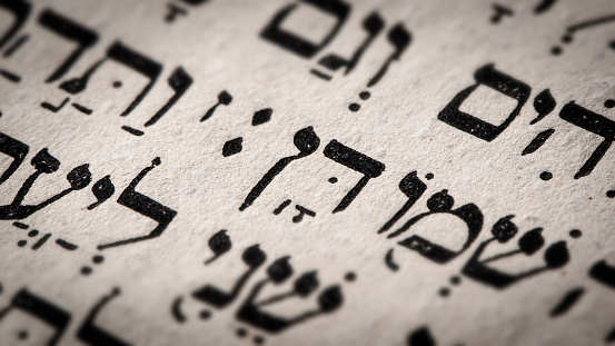 Hebrew word in Torah page. English translation is name Dan, the founder of the Israelite Tribe of Dan. First of the two sons of Jacob and Bilhah. Selective focus. Closeup