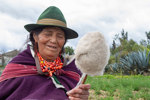 Cuenca, Ecuador - December 30, 2022: An elderly ecuadorian woman over 90 years old in typical clothes of Azuay province weaves and sells a straw basket.