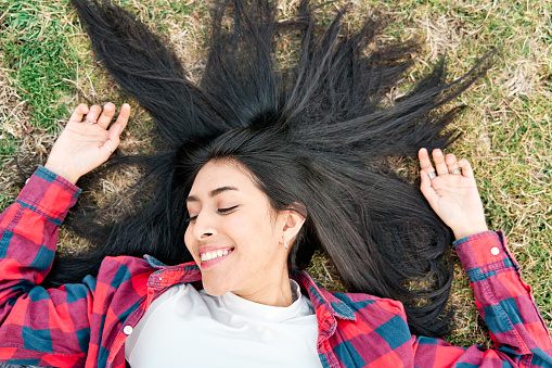 Young smiling Latina girl lying outdoors with her hair in the grass.