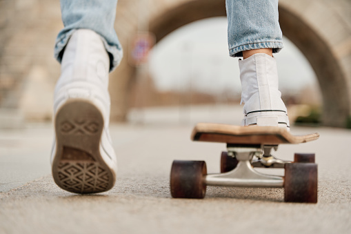 Close-up of a woman in white trainers and jeans skateboarding on a skateboard.