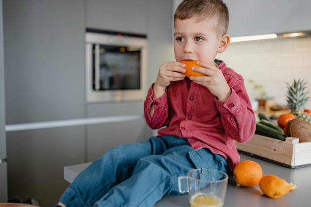 istock Cute little boy eating orange at home 1383994523