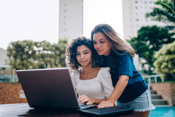 istock Mother and daughter using laptop at swimming pool area 1383996191