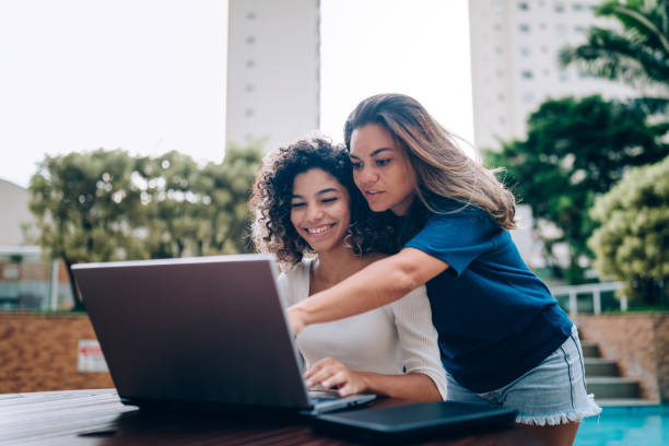 istock Mother and daughter using laptop at swimming pool area 1383996202