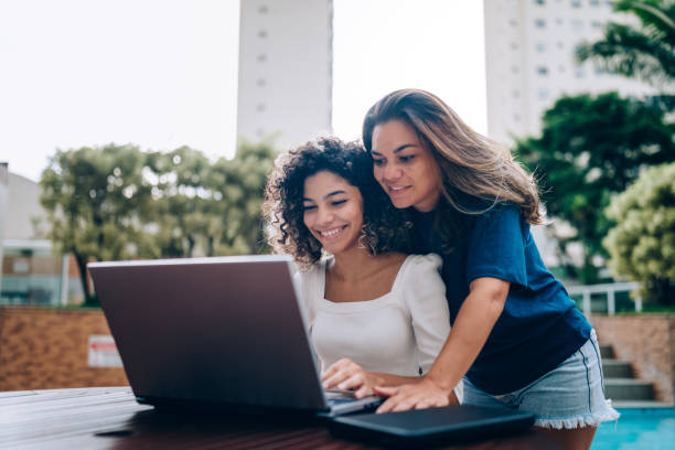 istock Mother and daughter using laptop at swimming pool area 1383996206
