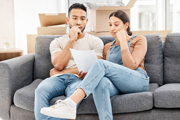 shot of a young couple looking worried and reading a letter while moving house - debt crisis fotos imagens e fotografias de stock