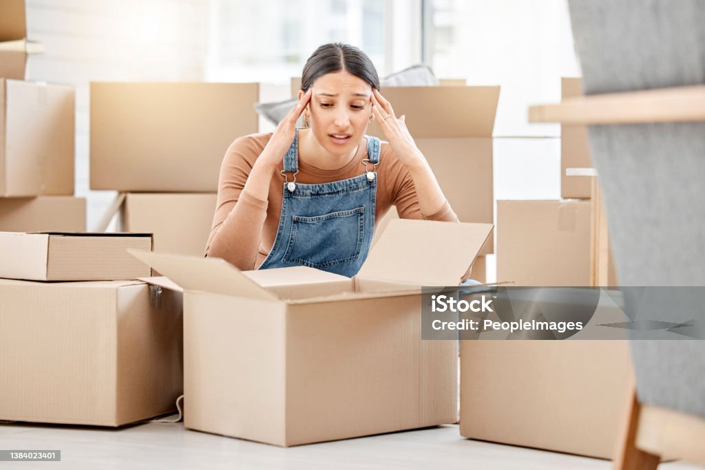 Shot of a young woman looking unhappy while moving house I have so much packing to do still Relocation Stock Photo