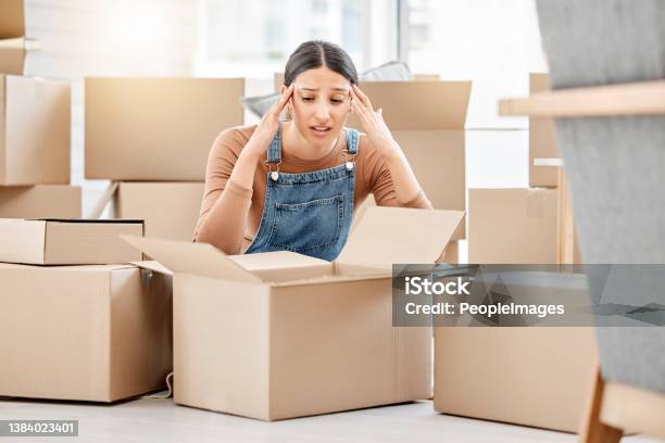 Shot Of A Young Woman Looking Unhappy While Moving House Stock Photo - Download Image Now
