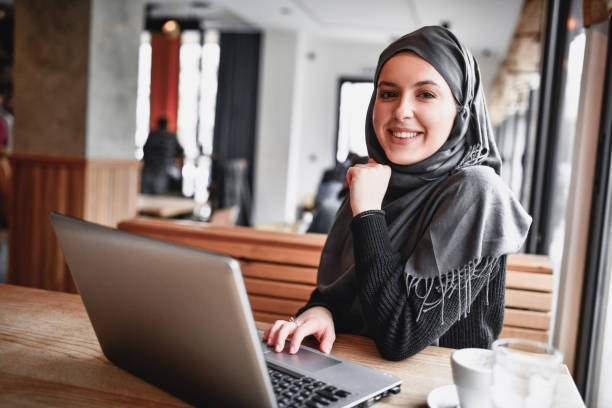 istock Smiling Muslim Female Using Laptop In Coffee Bar 1384032043