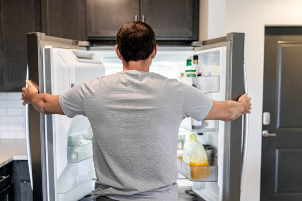 Back of hungry man opening fridge refrigerator doors domestic appliance searching for food inside with condiments and juice in modern kitchen stock photo