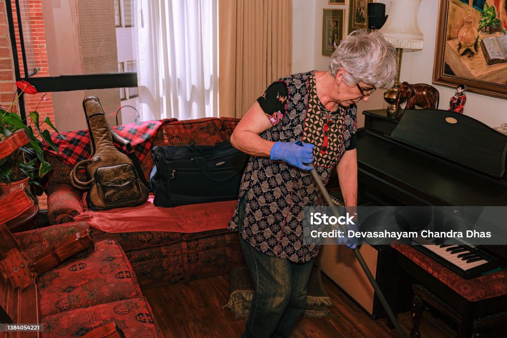 A Grey Haired Senior Latin American Lady Is Cleaning Her Living Room Before She Sets Up Her Christmas Tree A senior grey haired Colombian lady is seen cleaning her living room before she sets up her  Christmas tree for the holiday season. Horizontal format. 65-69 Years Stock Photo