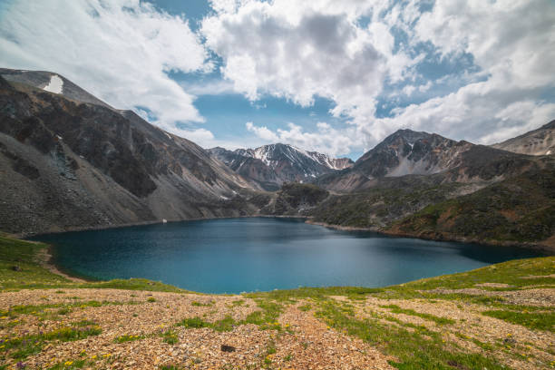 istock Deep mountain lake of phantom blue color among sharp rocks and high mountains in changeable weather. Wonderful dramatic view from sunlit grassy hill to deep blue alpine lake and rocks under cloudy sky 1384054579