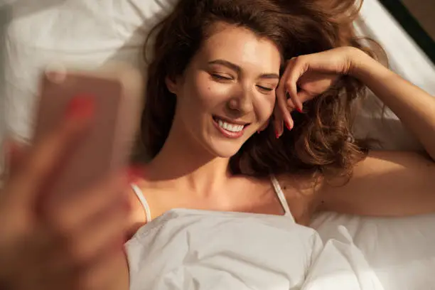 Photo of Young woman taking selfie in bed