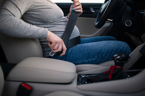 Unrecognisable pregnant woman adjusting seatbelt in a car.