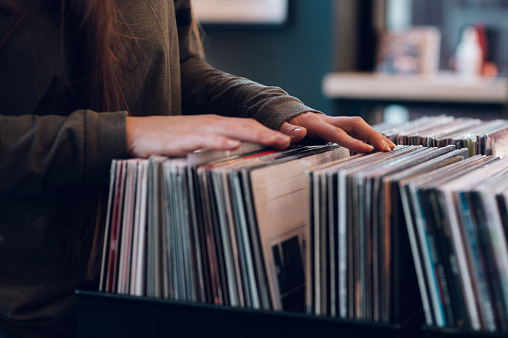 Close up of a woman hands choosing vinyl record in music record shop. Music addict concept. Old school classic concept. Focus on the hands and a vinyl record.