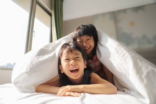 dwie azjatyckie dziewczyny bawiące się w kołdrę na łóżku. - child spring family little girls zdjęcia i obrazy z banku zdjęć